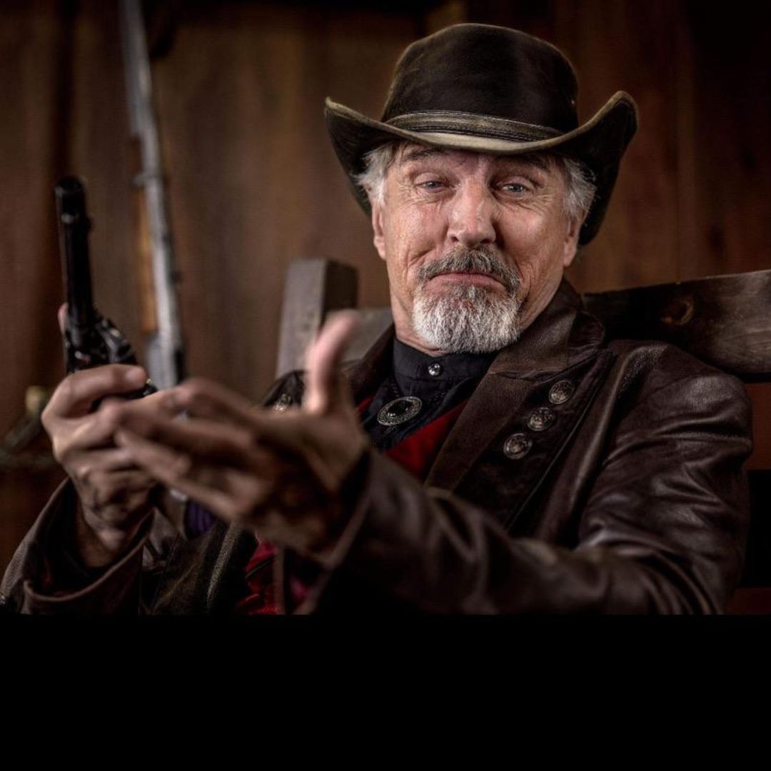 Nick Wilder als Emery Forster sitzend und Pistole in der rechten Hand haltend